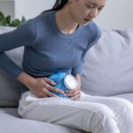 Nő hasi fájdalommal a kanapén ülve, egészségmegőrzés otthon.