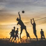Sportolók homokkupacban, naplementében strandröplabdázva.