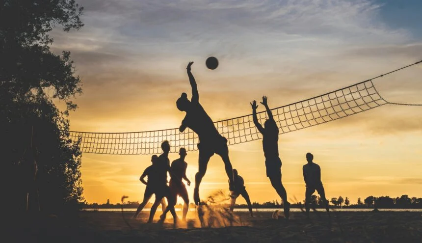 Sportolók homokkupacban, naplementében strandröplabdázva.